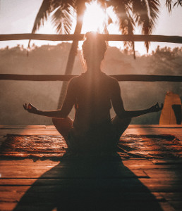 La méditation, un exemple de pratique spirituelle. Photo de femme de dos au lever de soleil en position méditative, illustrant l'article éveil et spiritualité