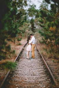 couple qui s'enlace au milieu de rails qui traversent une forêt