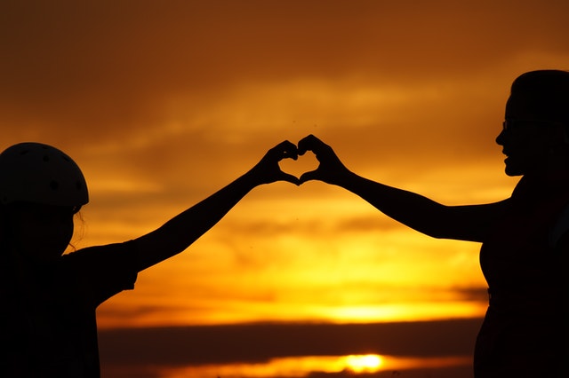 2 personnes relié en faisant un cœur avec leur main au coucher de soleil